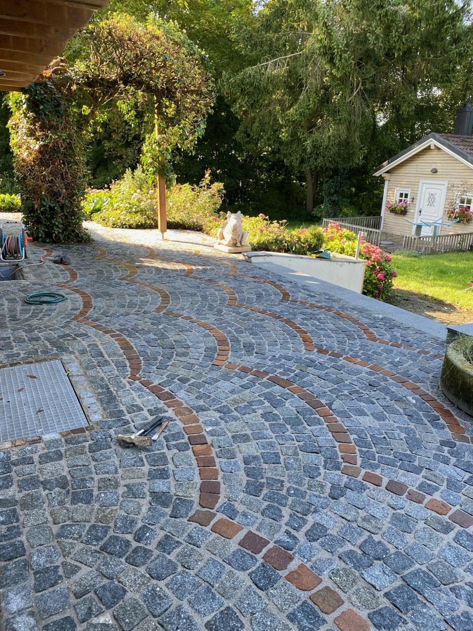 Terrasse aus Granitpflaster mit geschwungenen roten Bändern